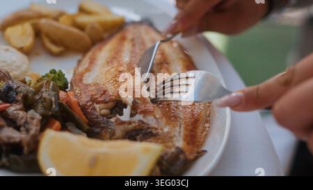 Persona che mangia pesce intero alla griglia con limone e verdure Foto Stock