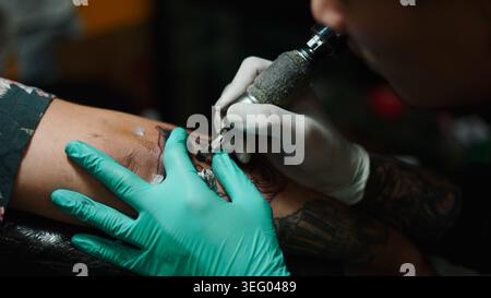 Tatuatore che lavora sul braccio di un cliente, creando body art personalizzati con la macchina Foto Stock