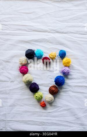 Composizione verticale di palline colorate disposte a forma di cuore su un morbido sfondo bianco testurizzato. Foto Stock