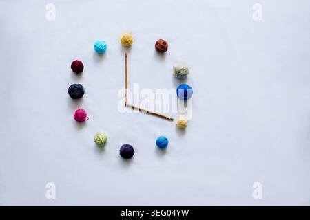 Orologio creativo realizzato con palline colorate in filato e ganci a uncinetto su uno sfondo bianco pulito. Foto Stock