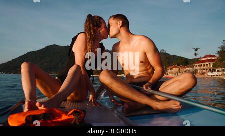 Coppia amorevole che condivide un bacio intimo in paddleboard durante le vacanze tropicali Foto Stock