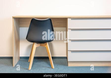 Scrivania in legno con sedia ergonomica in plastica scura e vista sul retro. Design minimalista. Interni moderni. Comodo luogo di lavoro con mobili. Tavolo con cassetti. Foto Stock