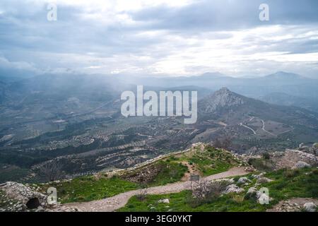 Un'ampia vista aerea cattura le antiche rovine di Akrokorint in Grecia, affacciato su un vasto paesaggio di oliveti, colline ondulate e lontane Foto Stock