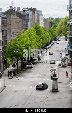 Vista verticale ad alto angolo delle infrastrutture immobiliari della città che mostra le auto di passaggio i cartelli stradali pedonali marciapiede e le facciate di vecchi edifici in mattoni in Lettonia Foto Stock