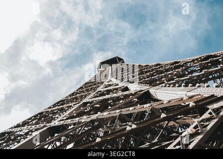 Ripresa dall'angolo basso della Torre Eiffel a Parigi, che enfatizza la sua complessa struttura in ferro contro un cielo blu, mostrando la miscela di architettura brilli Foto Stock