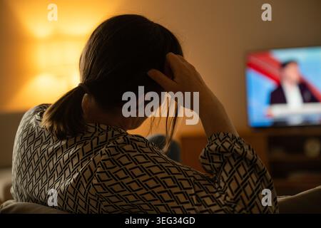 Donna seduta al chiuso di fronte allo schermo TV in camera buia, relax e moderno concetto di consumo multimediale, attenzione selettiva Foto Stock