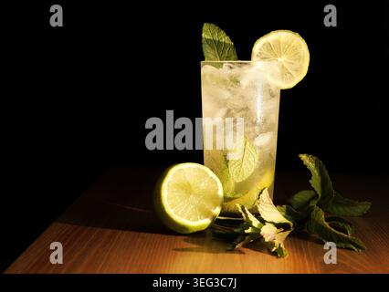 Cocktail Mojito con ghiaccio, fette di lime e foglie di menta fresca su un tavolo di legno, catturando l'essenza del rinfresco e delle bevande estive in a vi Foto Stock