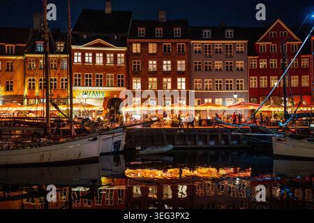 Una vibrante vista notturna di Nyhavn a Copenhagen. Le storiche case colorate sono illuminate e si riflettono sull'acqua del canale, dove sono ormeggiate le barche a vela. Foto Stock