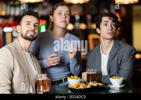 Gruppo di giovani amici entusiasti fan che tifanno squadra sportiva insieme, guardando la partita in TV al beer bar Foto Stock