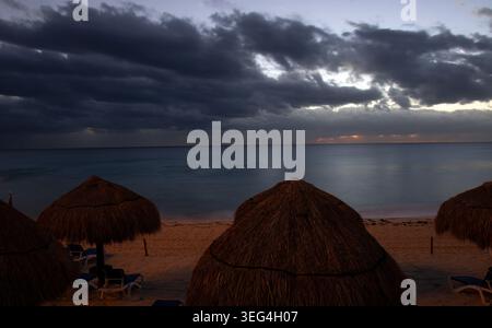 Nuvole scure nel cielo all'alba su una spiaggia con ombrelloni e sedie in una mattina invernale a Cancun, Messico. Foto Stock