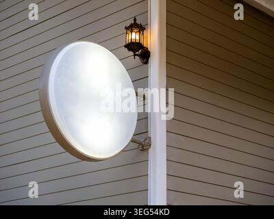 Cartello luminoso rotondo vuoto montato su parete in legno dell'edificio, ideale per il marchio di caffè o ristoranti. Mockup di cartellonistica aziendale, identità del punto vendita, all'aperto Foto Stock