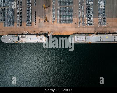 Due grandi navi da trasporto sono attraccate in un affollato terminal portuale per caricare file di nuove autovetture per l'esportazione e la logistica automobilistica internazionale. Foto Stock