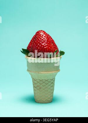 Un solo frutto di fragola rossa matura collocato all'interno di un cono di wafer semplice su sfondo blu Foto Stock