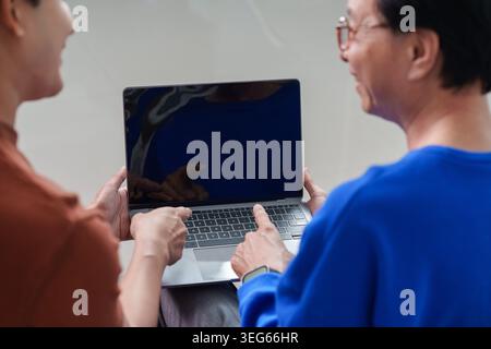 Uomo asiatico che insegna agli anziani come usare il laptop, l'apprendimento digitale intergenerazionale Foto Stock