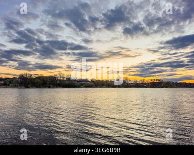 La luce dell'ora d'oro illumina il cielo e si riflette sulla superficie ondulata dell'acqua, emettendo un caldo bagliore sul paesaggio Foto Stock