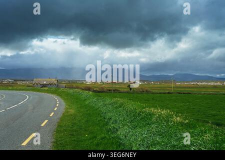 Spettacolare vista suggestiva di una strada che attraversa campi verdi nella contea di Kerry in Irlanda durante una tempesta estiva. Foto Stock