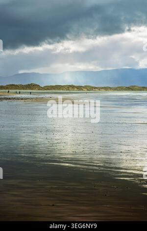 Spettacolare costa atlantica con bassa marea con increspature di sabbia bagnata e sagome di montagna sotto un cielo nuvoloso in Irlanda. Foto Stock