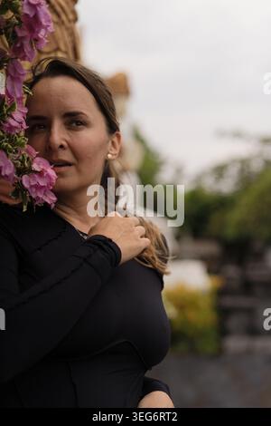 Donna matura penosa accanto a scultura balinese e fiori rosa, Bali Foto Stock