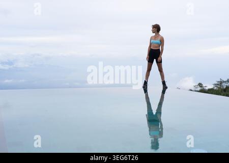 Donna sportiva che guarda l'orizzonte dall'infinity pool edge, Munduk, Bali Foto Stock