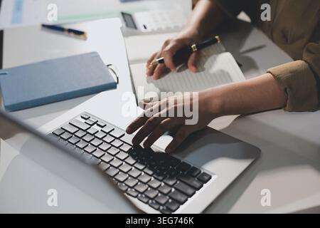Giovane donna asiatica che lavora fino a tardi alla sua scrivania, ha una videochiamata o una riunione online con un portatile, analizza i dati e gestisce i dati finanziari aziendali in un Foto Stock