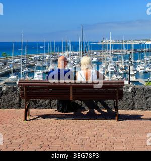 Coppia di mezza età seduta su una panchina con vista su Marina Rubicon, Playa Blanca, Lanzarote, Isole Canarie, Spagna, Europa Foto Stock