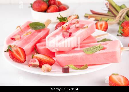 Papaveri per gelato al rabarbaro alla fragola. Sorbetto di frutta surgelato, gelato allo yogurt su bastoncini, con fragole purea, rabarbaro e succo di frutta, con ingredienti o Foto Stock