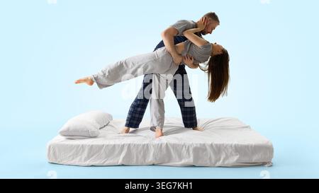 Uomo che immerge la donna all'indietro sul letto bianco da una vista laterale su sfondo blu. Foto Stock
