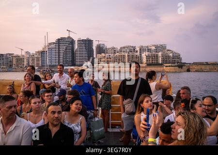 Un gruppo diversificato di persone si trova sul ponte di una barca nella zona dei traghetti di Sliema, Malta, 16 agosto 2025. L'immagine mostra i passeggeri Foto Stock