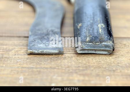 Due pezzi di una falce di ferro rotta poggiano fianco a fianco su una superficie rustica in legno. La vista ravvicinata rivela chiaramente il punto di frattura frastagliato in cui si trova Foto Stock