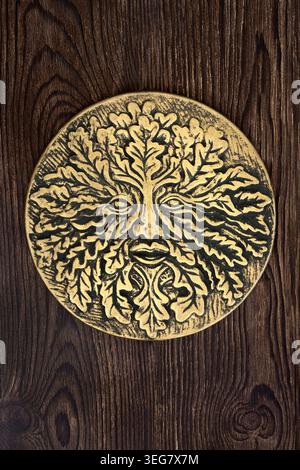 Decorazione a placca oro Green Man su legno rustico. Leggendaria figura naturale simbolo della rinascita nel folklore medievale, ciclo di vita dello spirito pagano degli alberi. Foto Stock