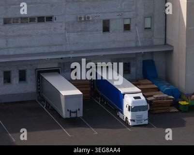 I camion merci sono parcheggiati presso le banchine di carico di un centro logistico per la distribuzione delle merci e le operazioni della catena di approvvigionamento. Foto Stock