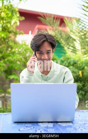 Ritratto verticale di un giovane uomo d'affari asiatico o di un lavoratore remoto della regione di Isan in Thailandia seduto all'aperto su una piastrella blu Foto Stock