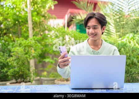 Un ritratto orizzontale dello stile di vita di un allegro giovane uomo d'affari asiatico o di un lavoratore remoto della regione di Isan in Thailandia seduto all'aperto in un'atmosfera blu Foto Stock