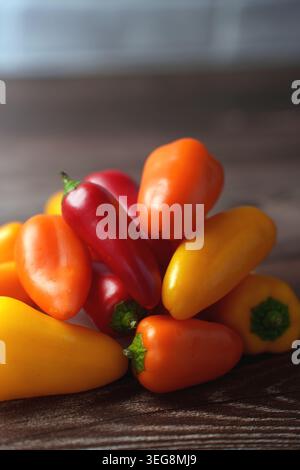 vibranti mini peperoni assortiti in una disposizione colorata su una superficie di legno scuro, che mostra sfumature contrastanti di rosso, giallo e arancio sotto di so Foto Stock