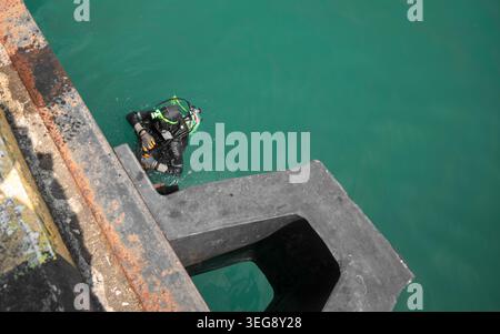Ripresa ad alto angolo di un subacqueo professionista in muta nera che ispeziona un molo in cemento Foto Stock