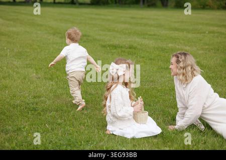 Un momento di gioia in famiglia catturato mentre i bambini giocano sull'erba mentre un adulto guarda, perfetto per le promozioni per la festa della mamma o per le campagne per la famiglia Foto Stock