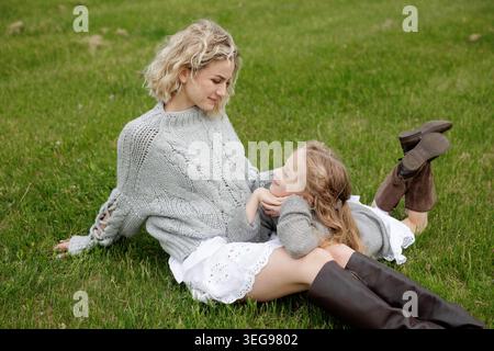 Una madre e una figlia gioiose condividono un momento di amore mentre si rilassano sull'erba, perfetto per campagne in famiglia o promozioni per la festa della mamma. Foto Stock