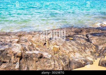 Il mare turchese lambisce dolcemente su una costa rocciosa con sabbia dorata a Khao Lak, Thailandia. spiaggia tropicale, vista oceano, paesaggio costiero. Foto Stock
