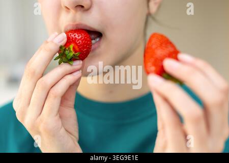 Persona che mangia fragole fresche da vicino. Primo piano di una persona che mangia fragole fresche, mostrando spuntini sani, frutta dolce e naturale ogni giorno Foto Stock