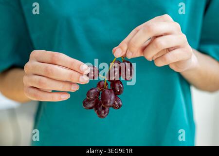 Mani che tengono da vicino uva rossa fresca. Primo piano di mani che tengono uva rossa fresca, mostrando spuntini sani, frutta naturale e semplice ogni giorno Foto Stock
