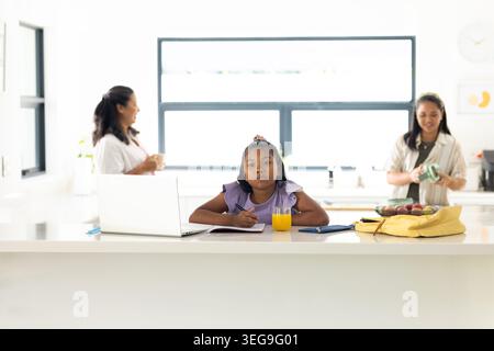 Diverse famiglie di donne in piedi, bambini seduti e che lavorano su un computer portatile nell'isola della cucina Foto Stock