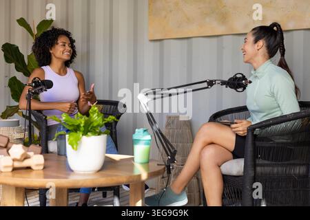 Diverse co-conduttrici femminili sedute in studio registrano podcast con microfoni e indossano abbigliamento sportivo Foto Stock