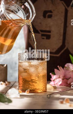 Versare il tè freddo in un bicchiere con cubetti di ghiaccio. Donna che prepara un tè freddo rinfrescante Foto Stock