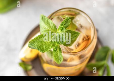 Tè al limone freddo con menta in vetro su sfondo grigio. Concetto di bevanda fresca e rinfrescante estiva Foto Stock