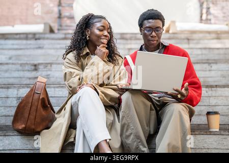 Felice coppia afroamericana studenti uomo e donna che studiano insieme guardando i media sul portatile. Foto Stock