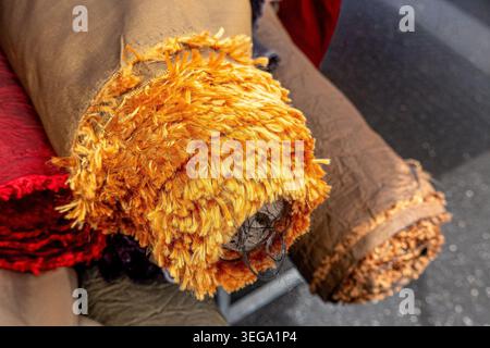 Rotolo di tessuto shaggy arancione vivace con la sua consistenza soffice e le frange esposte, che presenta diversi tessuti in rotoli pronti per progetti artigianali, moda, Foto Stock
