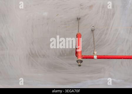 Tubo sprinkler antincendio rosso installato su un soffitto in calcestruzzo non finito che mostra le attrezzature di sicurezza dell'edificio in ambiente edile Foto Stock