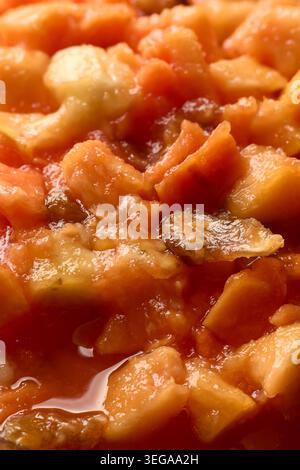 primo piano di insalata di frutta fresca mista con banane di papaia d'arancia tritate e uvetta sciroppata, superficie lucida con succosi pezzi di frutta dolce, full frame Foto Stock