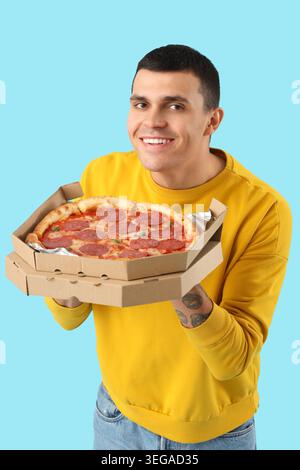 Giovane con gustosa pizza al peperoni su sfondo blu Foto Stock