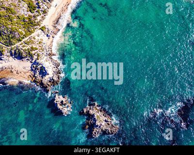 Splendida vista aerea che cattura una costa rocciosa che incontra acque turchesi cristalline. La spiaggia presenta sabbia dorata circondata da vegetazione lussureggiante, Foto Stock